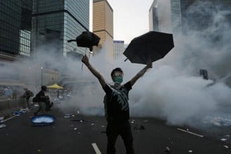 A protester raises his umbrellas in front of tear gas which was fired by riot police to disperse protesters blocking the main street to the financial Central district outside the government headquarters in Hong Kong