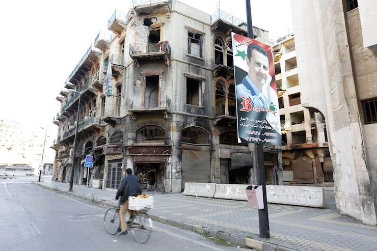 A man rides a bicycle past a poster depicting Syria's President Bashar al-Assad near the new clock square in the old city of Homs