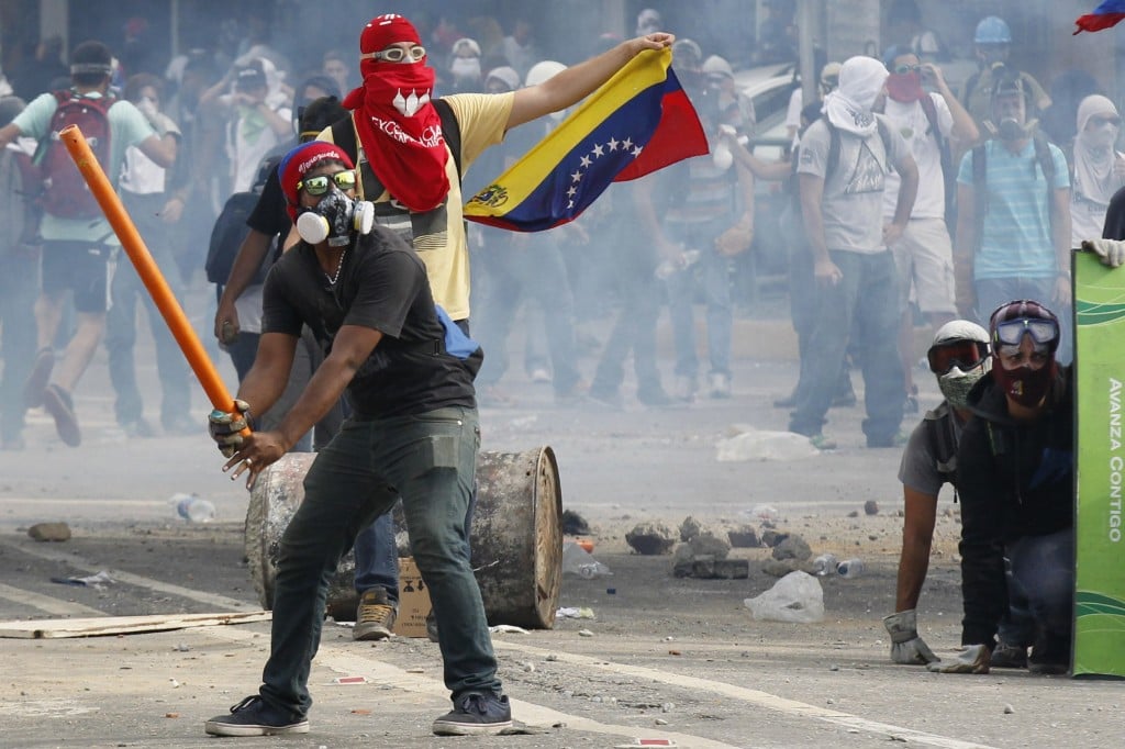 Anti-government demonstrators pretend to bat gas canisters to police during riots in Caracas