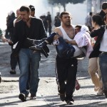 Injured Kurdish protester is carried by his friend as they clash with riot police in Diyarbakir