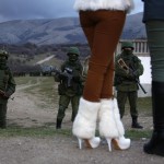 Local women watch armed men, believed to be Russian soldiers, assemble near a Ukrainian military base in Perevalnoe
