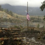 A flag flies at half-staff on a log with the slope of the massive mudslide that struck Oso in the background near Darrington, Washington