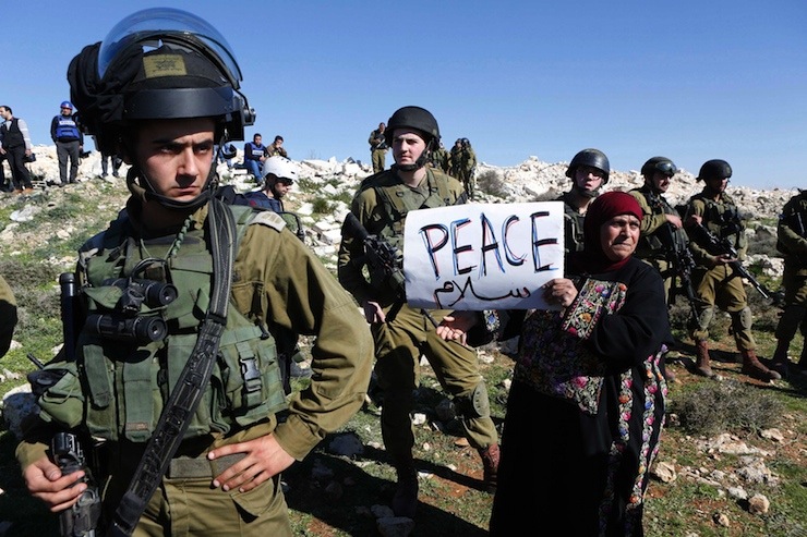 protester holds a placard as she stands next to Israeli soldiers during a protest against Israeli settlements in Beit Fajjar town south of the West Bank city of Bethlehem