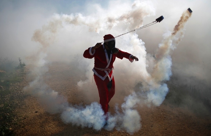 Palestinian protester, dressed as Santa Claus, uses a slingshot to return a tear gas canister fired by Israeli troops in the West Bank village of Bilin