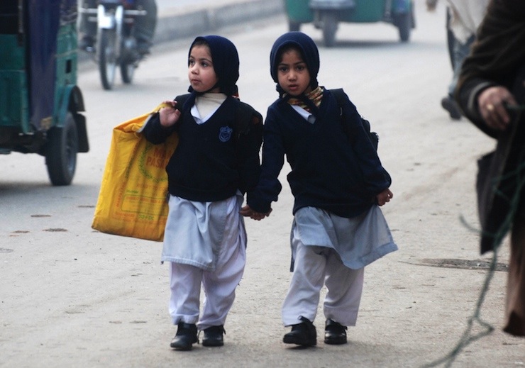 Girls carry their school bags as they walk along a road while heading to their school after it reopened in Peshawar