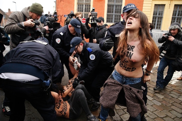 Police remove from the scene topless activists of women's rights group FEMEN as former IMF head Strauss-Kahn arrives to attend the trial on the so-called "Carlton Affair", in Lille