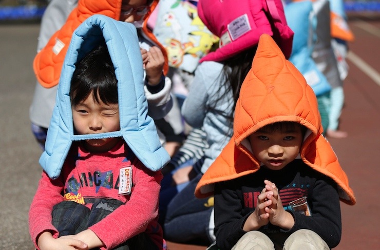 School children wearing padded hoods to protect them from falling debris sit on a playground during an earthquake simulation exercise at an elementary school in Tokyo