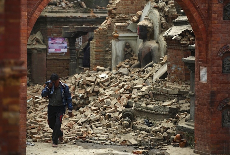 Man cries as he walks on the street while passing through a damaged statue of Lord Buddha a day after an earthquake in Bhaktapur