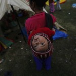 An earthquake victim carries her baby on her back as she stands outside her makeshift shelter on open ground in the early hours in Kathmandu