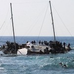 Migrants, who are trying to reach Greece, are seen onboard a capsized sailboat, as others are seen in the water trying to reach the coast of the southeastern island of Rhodes