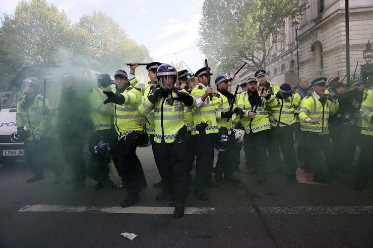 Police officers raise their batons as a smoke bomb goes off at the gates of Downing Street during a protest against the Conservative Party in central London