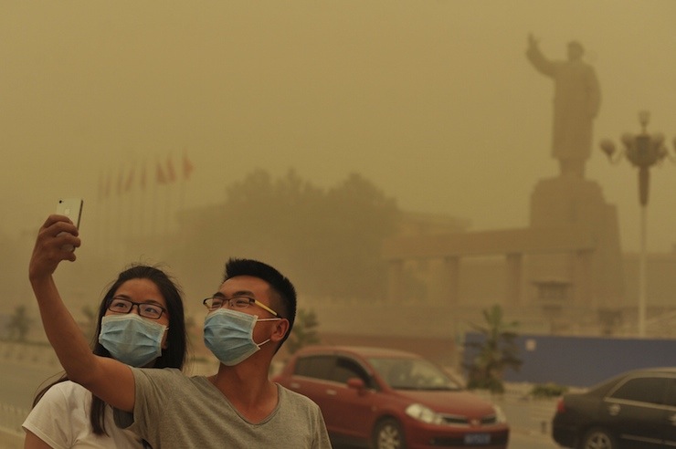 Residents wearing masks pose for a photograph near a statue of late Chinese Chairman Mao Zedong, as a sandstorm hits Kashgar
