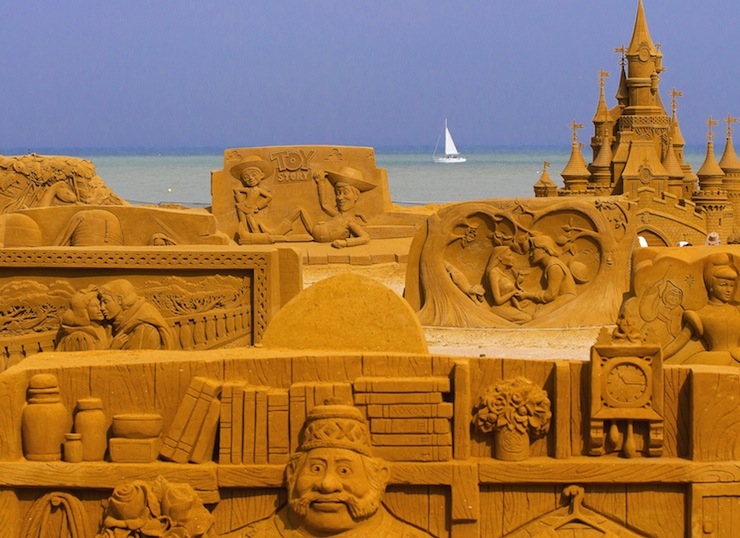 A sailing boat is seen behind sand sculptures during the Sand Sculpture Festival Frozen Summer Fun in Ostend