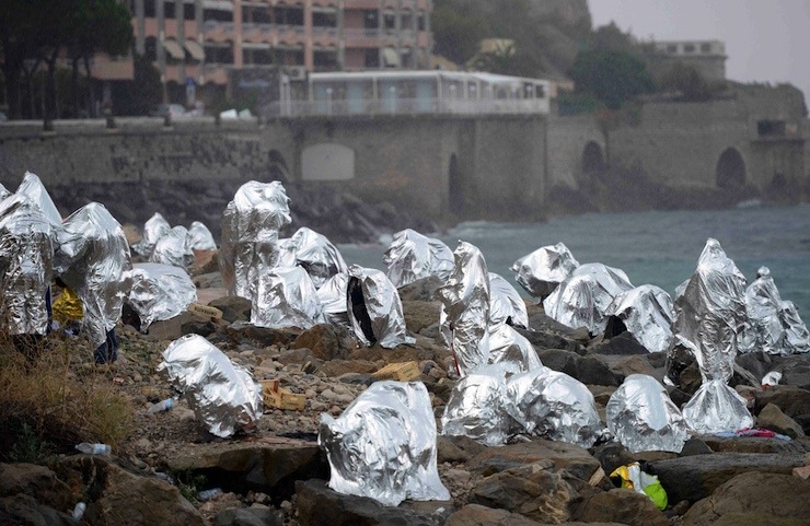 A group of migrants  protect themselves from the weather with emergency blankets on the seawall at the Saint Ludovic border crossing on the Mediterranean Sea between Vintimille, Italy and Menton