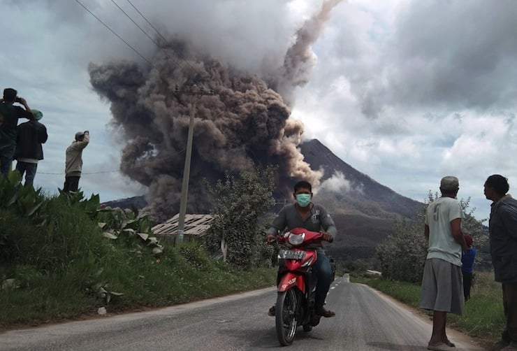 A resident rides his motorcycle as Mount Sinabung spews ash at Namanteran village in Karo Regency