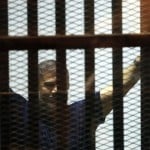 Former Egyptian President Mohamed Mursi waves during his appearance in court on the outskirts of Cairo, Egypt