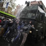 Students shout slogans as a riot police vehicle releases a jet of water during a demonstration to demand changes in the education system, in Santiago