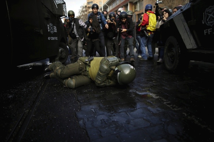 A policeman lies on the ground during a clash with students demonstrating to demand changes in the education system, in Santiago