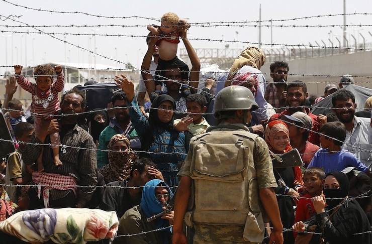 Syrian refugees wait behind the border fences to cross into Turkey at Akcakale border gate in Sanliurfa province, Turkey