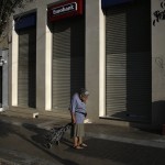 A woman pulling a shopping cart reacts outside a closed Eurobank branch in Athens