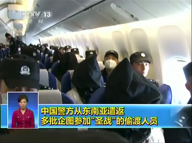 Still image taken from video shows people being deported from Thailand seated in an airplane flanked by police at an unidentified location in China