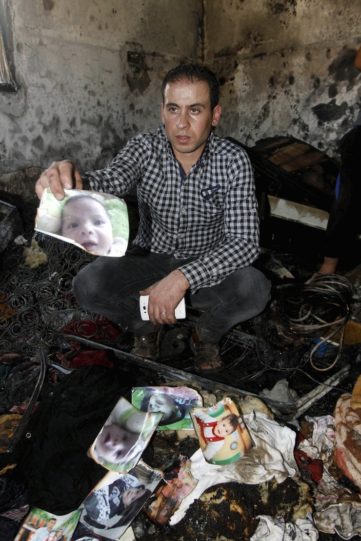 A relative of 18-month-old Palestinian baby Ali Dawabsheh, who was killed after his family's house was set to fire in a suspected attack by Jewish extremists, shows his picture at the burnt house in Duma village near the West Bank city of Nablus July 31, 2015. Suspected Jewish extremists set fire to a Palestinian home in the occupied West Bank on Friday, killing Dawabsheh and seriously injuring several other family members, an act that Israel's prime minister described as terrorism. REUTERS/Abed Omar Qusini