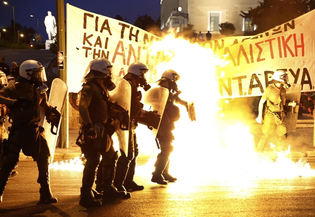 Riot police stand amongst flames from petrol bombs thrown by a small group of anti-establishment demonstrators in Athens