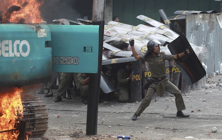 A municipal police officer throws a stone back at protesting residents of Kampung Pulo after clashes erupted during an eviction in Jakarta