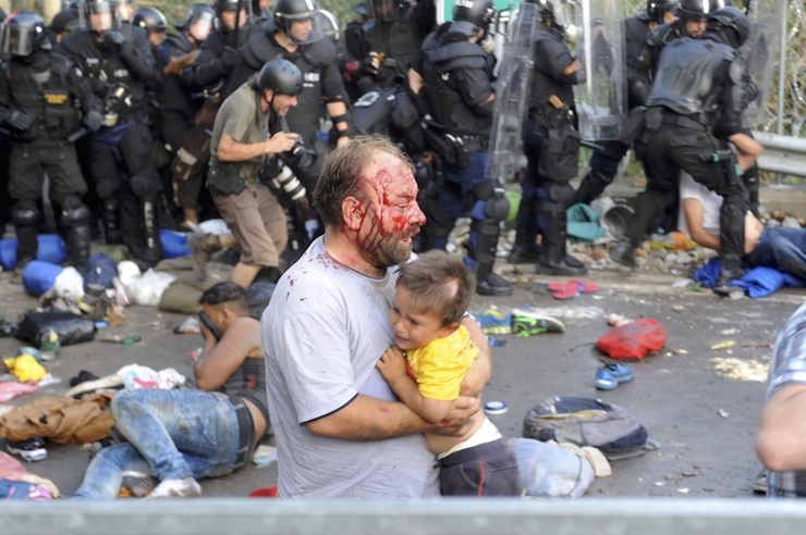An injured migrant carries a child during clashes with Hungarian riot police at the border crossing with Serbia in Roszke, Hungary September 16, 2015. Hungarian police fired tear gas and water cannon at protesting migrants demanding they be allowed to enter from Serbia on Wednesday on the second day of a border crackdown. REUTERS/Karnok Csaba TPX IMAGES OF THE DAY