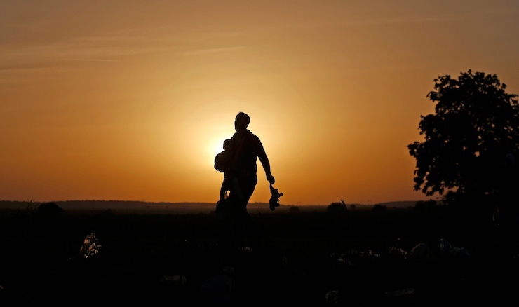 A migrant carries a child and a toy as he approaches the Croatian border near the town of Sid