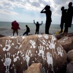 A group of Sudanese and Eritrean migrants are seen in silhouette near a rock with white hand prints on the seawall at the Saint Ludovic border crossing on the Mediterranean Sea between Vintimiglia and Menton