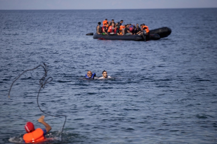 A man throws a rope to Syrian refugees swimming towards a beach after abandoning a dinghy with a broken engine on the Greek island of Lesbos
