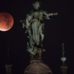 The moon, appearing in a dim red colour, is covered by the Earth's shadow during a total lunar eclipse over a staute at the roof of the town hall in Hamburg