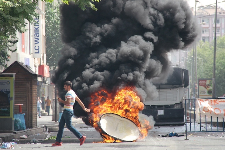 Man runs past a burning trash can, set on fire by protesters before a police vehicle, in the Kurdish dominated southeastern city of Diyarbakir, Turkey
