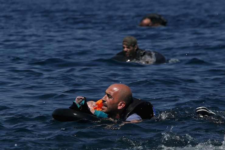 Syrian refugee holding a baby in a lifetube swims towards the shore after their dinghy deflated some 100m away before reaching the Greek island of Lesbos