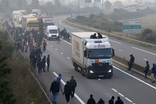 Migrants gather on the road as others board lorries that queue on the access road to reach the ferry terminal in Calais, France, October 3, 2015. Overnight around 200 migrants tried to get into the Channel Tunnel in France, clashing with staff and police and forcing the suspension of rails services a spokesman for Eurotunnel said. Around 3,000 migrants fleeing war and poverty in Africa and the Middle East are camped on the French side of the tunnel in Calais, trying to board vehicles heading for Britain via the tunnel and on ferries or by walking through the tunnel, even though security measures aimed at keeping them out have been stepped up. REUTERS/Pascal Rossignol