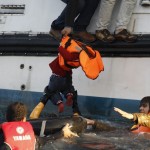 A refugee hands over a toddler to a volunteer lifeguard as a half-sunken catamaran carrying around 150 refugees, most of them Syrians, arrives after crossing part of the Aegean sea from Turkey on the Greek island of Lesbos