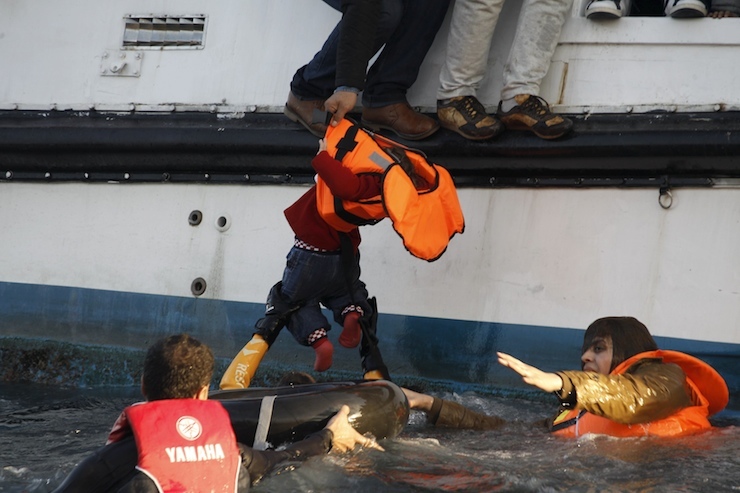 A refugee hands over a toddler to a volunteer lifeguard as a half-sunken catamaran carrying around 150 refugees, most of them Syrians, arrives after crossing part of the Aegean sea from Turkey on the Greek island of Lesbos