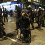 A protester on a wheelchair wearing a gas mask is seen next to a riot police cordon during clashes in Athens