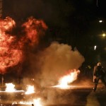 A petrol bomb explodes next to a riot police officer during clashes with hooded youth in Athens