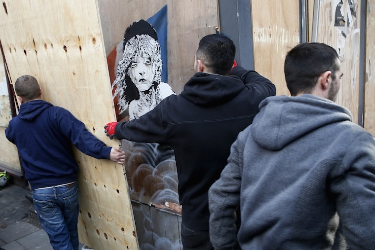 Workers remove a board after uncovering a new graffiti mural attributed to Banksy, opposite the French embassy in London, Britain January 25, 2016. A mural by British graffiti artist Banksy highlighting the alleged use of tear gas on migrants from the "jungle" camp in Calais has appeared on a hoarding near the French embassy in London. REUTERS/Stefan Wermuth EDITORIAL USE ONLY. NO RESALES. NO ARCHIVE.