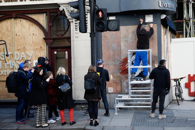 A worker tries to remove a new graffiti mural attributed to Banksy, opposite the French embassy in London, Britain January 25, 2016. A mural by British graffiti artist Banksy highlighting the alleged use of tear gas on migrants from the "jungle" camp in Calais has appeared on a hoarding near the French embassy in London. REUTERS/FOR EDITORIAL USE ONLY. NO RESALES. NO ARCHIVES.