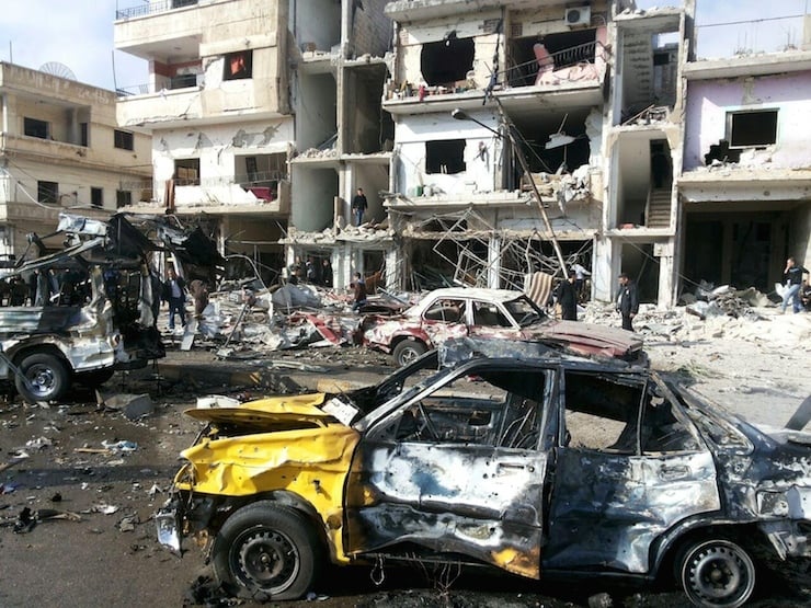 People inspect the site of a two bomb blasts in the government-controlled city of Homs