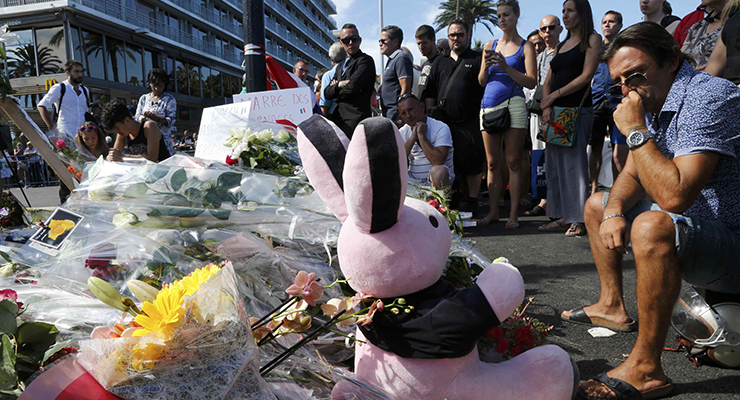 People gather near flowers, candles and a stuffed toy as they pay tribute near the scene where a truck ran into a crowd at high speed killing scores and injuring more who were celebrating the Bastille Day national holiday in Nice