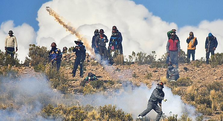 An independent miner returns a tear gas capsule during clashes with riot police during a protest in Panduro
