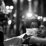 Two women embrace while looking at a police officer in uptown Charlotte, NC during a protest of the police shooting of Keith Scott, in Charlotte