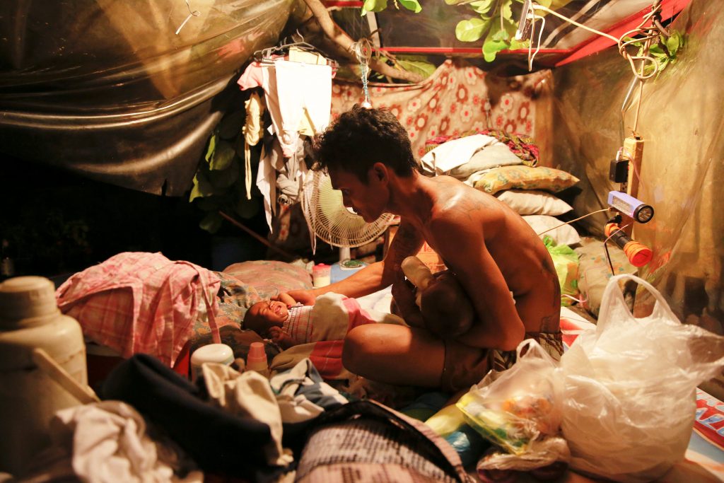 A man who lives with his family in a tent erected atop a tombstone, feeds his two-month old twins at the North Cemetery where many victims of the country's war on drugs are buried, in Manila, Philippines October 16, 2016. REUTERS/Damir Sagolj