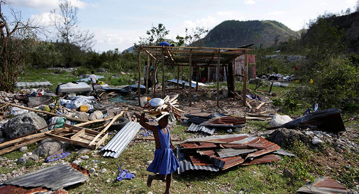 A girl carrying wood walks near debris after Hurricane Matthew passed, in Camp Perrin