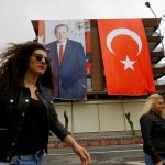 People walk past by a building which is decorated by a poster of Turkish President Erdogan and a Turkish flag before a rally for the upcoming referendum in the Kurdish-dominated southeastern city of Diyarbakir