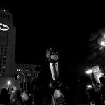 A person wearing a Batman costume poses for photos as a bat-signal is projected on City Hall in honor of late actor Adam West in Los Angeles